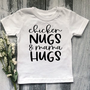 May include: White short-sleeved t-shirt with black text that reads "chicken NUGS & mama HUGS".