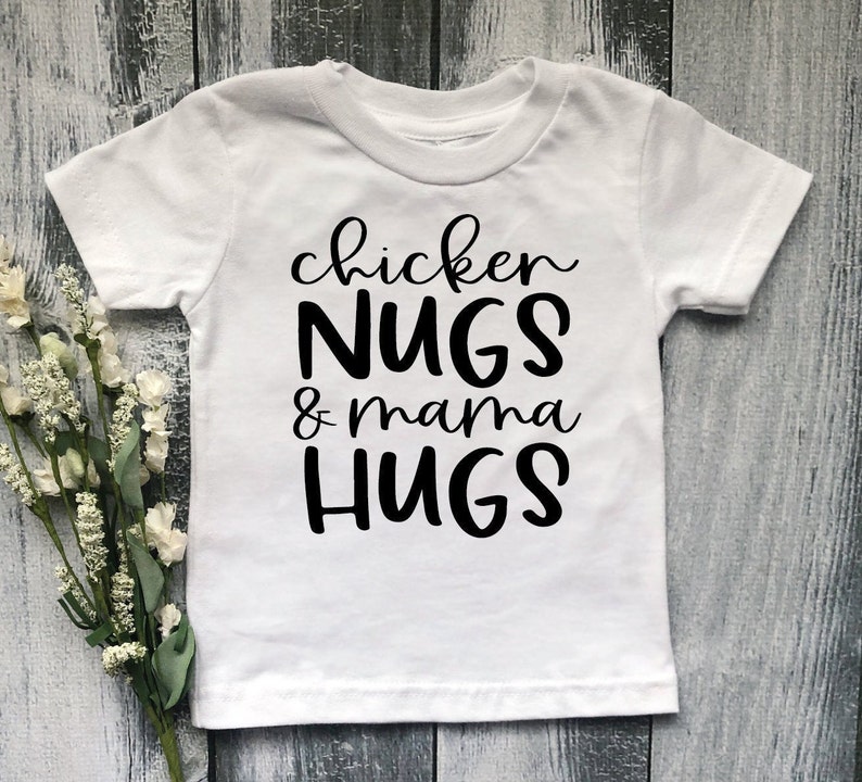 May include: White short-sleeved t-shirt with black text that reads "chicken NUGS & mama HUGS".