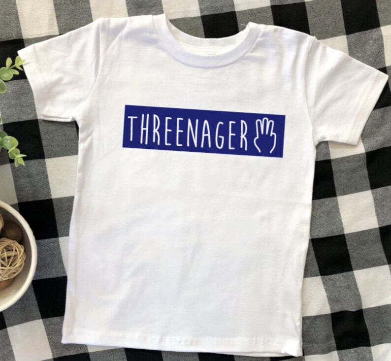 May include: White t-shirt with a blue rectangle that says "THREEENAGER" with a hand drawn three fingered hand.