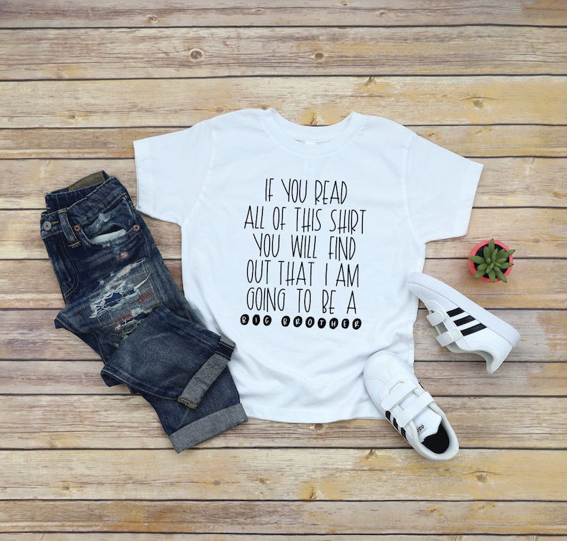 May include: White t-shirt with black text that reads "If you read all of this shirt you will find out that I am going to be a big brother."