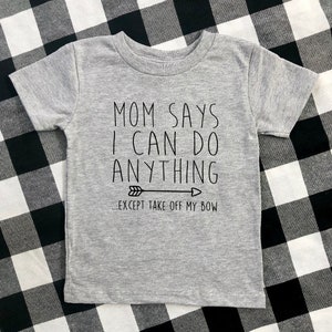 May include: Gray short-sleeved t-shirt with black text that reads "Mom says I can do anything... except take off my bow" with a black arrow pointing to the right.