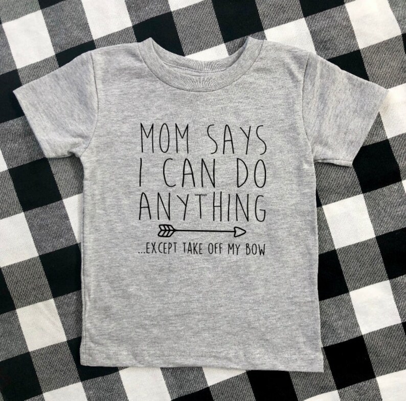 May include: Gray short-sleeved t-shirt with black text that reads "Mom says I can do anything... except take off my bow" with a black arrow pointing to the right.