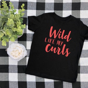 May include: Black t-shirt with the text "Wild Like My Curls" in red lettering.