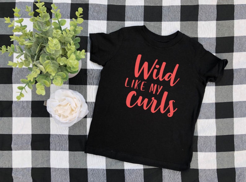 May include: Black t-shirt with the text "Wild Like My Curls" in red lettering.