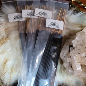 May include: Four packs of incense sticks in clear plastic packaging. The incense sticks are black and have a gold-colored string attached to the top. The packaging has labels with the names of the scents: "Trippy Hippie", "Sea Witch", "Dragon's Blood", and "Spice Cabinet".