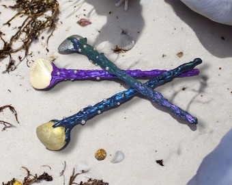 May include: Two iridescent spoons with seashell bowls and pearl accents. The spoons are crossed and lying on a white sandy surface.