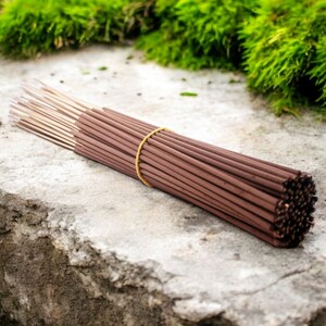 May include: A bundle of brown incense sticks tied together with a yellow rubber band. The sticks are arranged in a circular shape and are lying on a gray concrete surface.