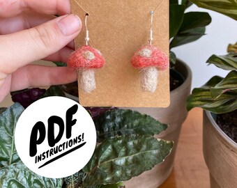 Peut inclure: Boucles d'oreilles champignons faites à la main, avec des chapeaux rouges et des points blancs, suspendues à des crochets argentés. Les boucles d'oreilles sont présentées sur une carte marron. Le texte "PDF INSTRUCTIONS!" est visible.
