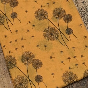 May include: A yellow fabric with a repeating pattern of black dandelion flowers. The fabric has a slightly textured surface.