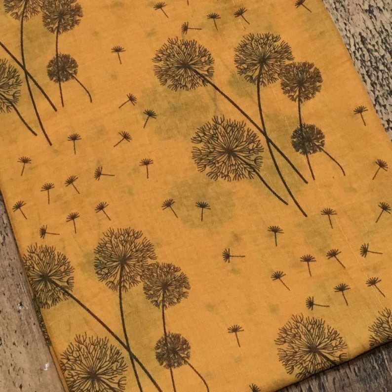 May include: A yellow fabric with a repeating pattern of black dandelion flowers. The fabric has a slightly textured surface.