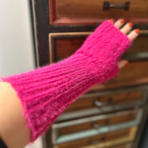 Peut inclure: Un gant sans doigts fuchsia vif, fabriqué à partir d'un matériau doux et texturé. Le gant couvre le poignet et l'avant-bras, avec un design en tricot côtelé. La couleur rose vif est accrocheuse.