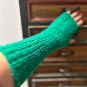 Peut inclure: Un gant sans doigts vert vif en tissu tricoté côtelé texturé. Le gant couvre l'avant-bras et laisse les doigts exposés. La couleur est un vert vif et uni, et le tricot a un aspect légèrement flou.