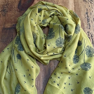 May include: A green scarf with a dandelion print. The dandelions are black and have a wispy design.