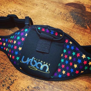 May include: Black fitness belt with a pattern of colourful stars. The belt features a small pocket and the words "Urban Fitness". It has a black buckle and strap.
