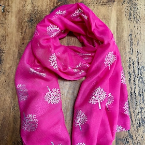 May include: A pink scarf with a silver tree pattern. The scarf is folded and laid out on a wooden surface.