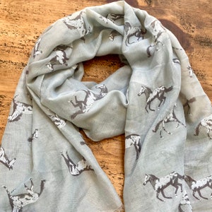 May include: A light gray scarf with a repeating pattern of white horses. The scarf is made of a soft, lightweight fabric and is perfect for adding a touch of elegance to any outfit.