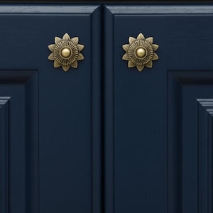 May include: Two antique brass cabinet knobs shaped like stylized flowers with layered petals and a central dome, mounted on a pair of dark navy blue cabinet doors featuring a recessed panel design with clean, straight edges and a smooth finish.