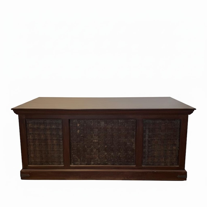May include: A rectangular wooden desk with a dark brown finish. The front panel features three distinct sections, each containing a dark, textured grid pattern. The desk has a flat, smooth top surface and a solid base with small metal accents.