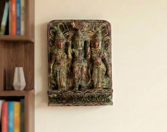 May include: A rectangular wooden wall plaque featuring a carved relief of three figures standing side by side. The sculpture displays a weathered finish with tones of brown, green, and gold, showcasing intricate details on the clothing and jewelry.