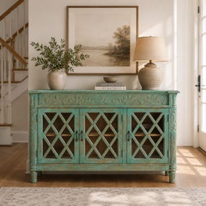 May include: A rectangular turquoise sideboard with a distressed finish, featuring three cabinet doors with a diamond lattice pattern, carved floral details along the top edge, and fluted side columns, standing on four short, turned wooden feet.