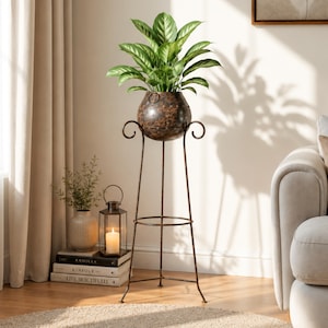 May include: A tall, dark brown metal plant stand with a spherical, riveted planter bowl at the top. The stand features slender legs, a circular support ring, and decorative scrolled accents. A lush green plant with pointed leaves sits inside the bowl.