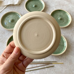 May include: A set of five ceramic incense holders. The holders are round and have a green glaze with a white swirl design. One holder is shown upside down, revealing a beige unglazed bottom.