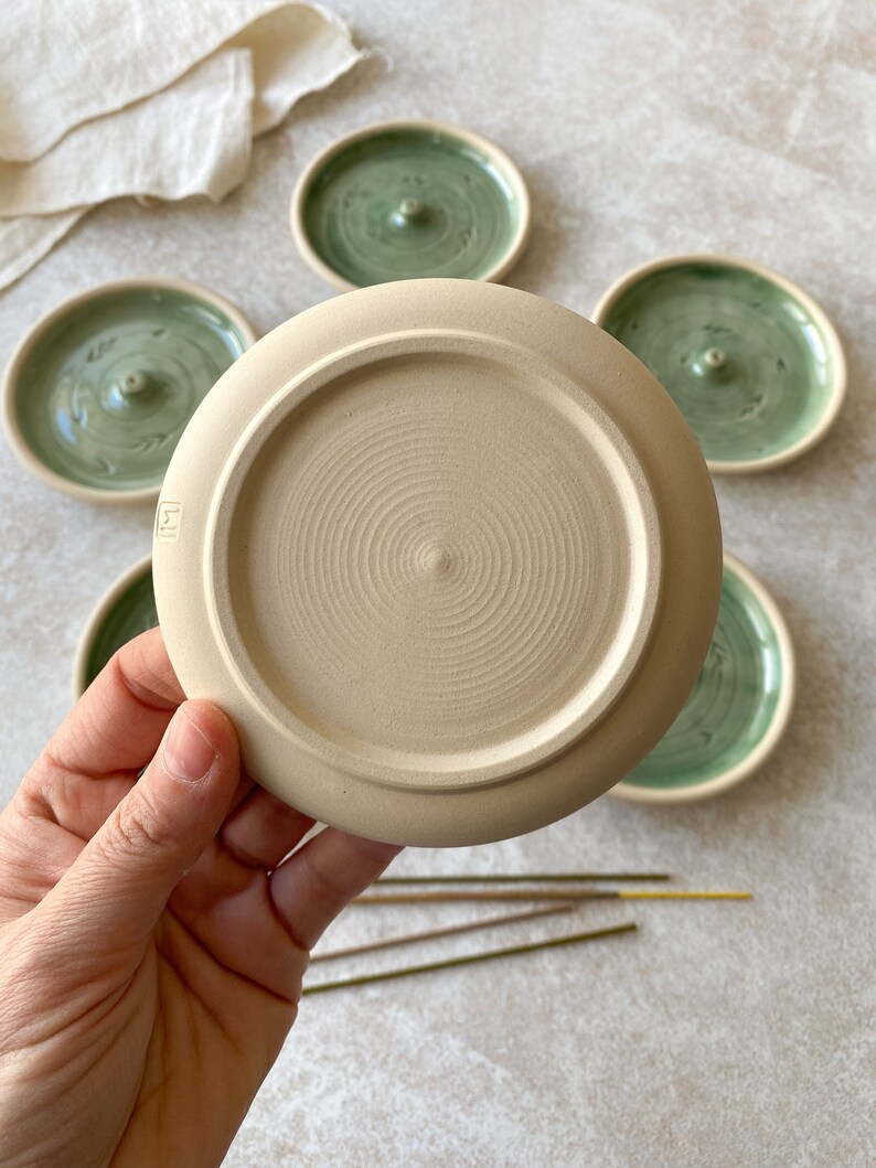 May include: A set of five ceramic incense holders. The holders are round and have a green glaze with a white swirl design. One holder is shown upside down, revealing a beige unglazed bottom.