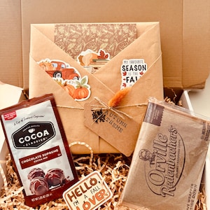 May include: A fall-themed gift box filled with cocoa mix, gourmet popcorn, and decorative stickers. The box includes a kraft paper envelope with autumn-themed stickers and a tag that reads "Autumn Theme". The sticker says "Hello I'm a Fall Lover".