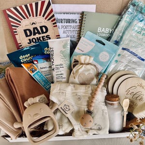 May include: A gift basket filled with baby and postpartum essentials. Includes a "Dad Jokes" book, baby logbook, baby clothes, a teething toy, and skincare products. Also includes a perineal cold pack and wooden coasters.