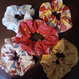 May include: Five colorful hair scrunchies with cartoon pig designs. The scrunchies are made of soft fabric and are perfect for holding hair in place.