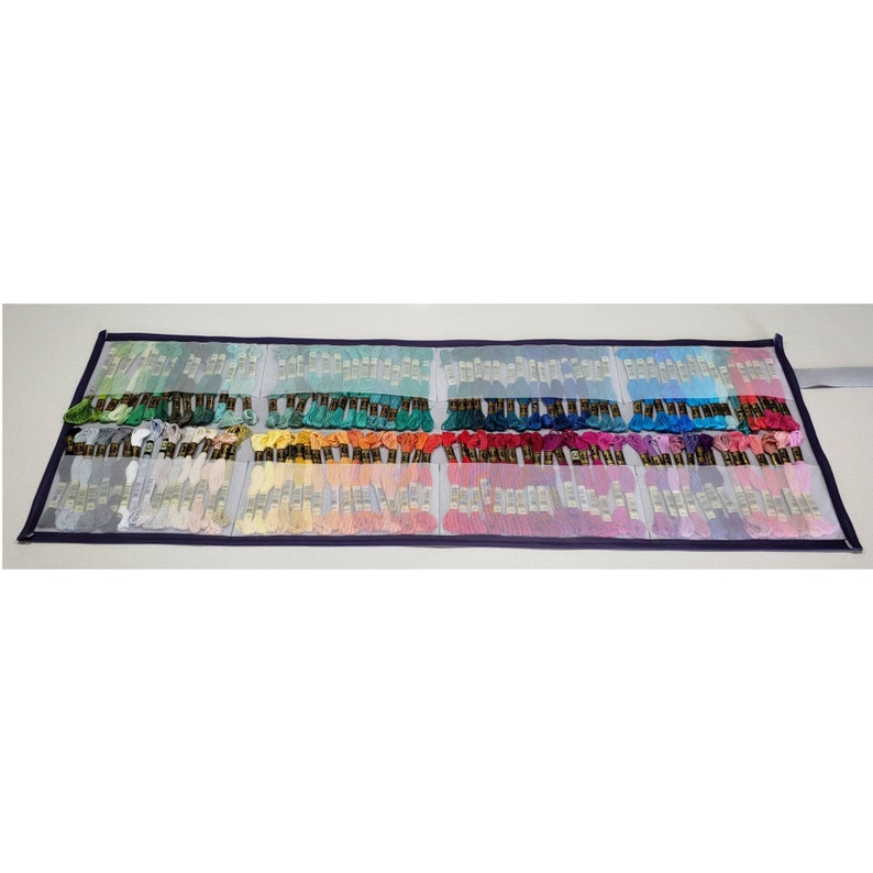 以下が含まれることがあります： 青い縁取りのある白いメッシュ収納ケースには、さまざまな色の刺繍糸の糸巻きが入っています。糸巻きは、行と列に整理されており、虹色の効果を生み出しています。