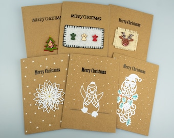Puede incluir: Seis tarjetas de Navidad hechas a mano. Cada una es de cartulina marrón con la frase "Merry Christmas" en negro. Decoradas con elementos festivos: un árbol, ángeles, un reno, una flor, un pingüino y un búho. Diseño rústico.