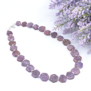 May include: A purple gemstone necklace with silver accents. The necklace is made of faceted, hexagonal beads and is strung on a silver chain.