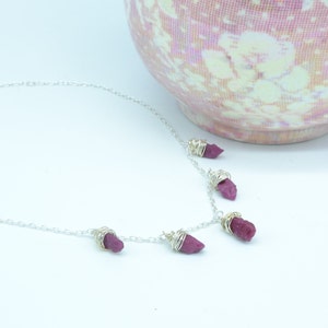 May include: A silver chain necklace with five dangling pink ruby stones wrapped in silver wire.