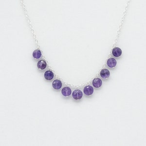 Könnte beinhalten: Eine silberne Kettenkette mit einer Reihe von baumelnden Amethystperlen. Die Perlen sind rund und facettiert und haben eine tiefviolette Farbe.