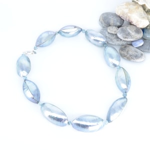 May include: A light blue pearl necklace with oval-shaped pearls. The necklace is on a white background.