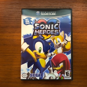Puede incluir: Una caja de juego de video para Nintendo GameCube con Sonic el Erizo, Knuckles el Equidna y Tails el Zorro. El juego se llama "Sonic Heroes" y tiene el texto "All New Sonic!" en la portada.