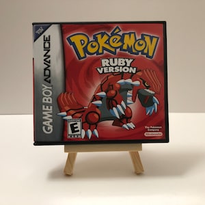 May include: A Game Boy Advance video game cartridge for Pokémon Ruby Version. The game case is black with a red and white design featuring a red and white creature. The game is rated E for Everyone.