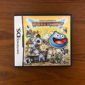 May include: A Nintendo DS game case for "Dragon Quest Heroes: Rocket Slime." The cover art features a large blue slime character with a wide grin, set against a backdrop of a cartoonish castle and other characters. The game case is on a wooden surface.