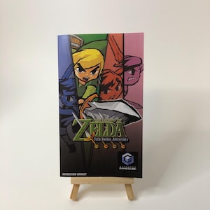 Op de afbeelding: Instructieboekje voor The Legend of Zelda: Four Swords Adventures voor de Nintendo GameCube. De cover toont vier stripfiguren met zwaarden, in tinten blauw, groen, oranje en paars. De titel is in groen en goud.
