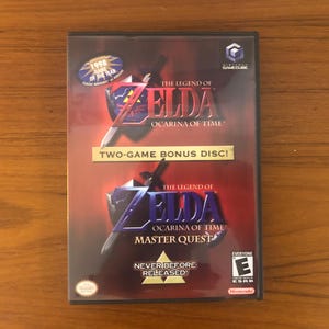 May include: A GameCube video game case for "The Legend of Zelda: Ocarina of Time" with a "Two-Game Bonus Disc!" label. The case has a red and black background with the game's logo and "Master Quest" text.