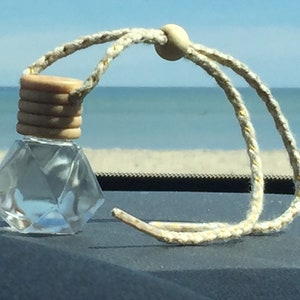 May include: A clear glass car air freshener with a diamond-shaped design and a wooden cap. The air freshener is hanging from a beige string with a wooden bead.