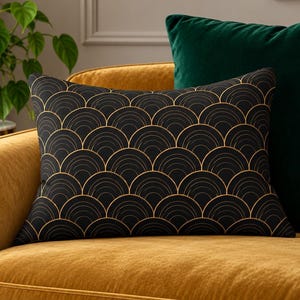 May include: A rectangular throw pillow featuring a black fabric base with a repeating gold-colored fan-shaped arc pattern. The pillow is positioned on a mustard yellow upholstered sofa, accompanied by a solid dark green velvet cushion.
