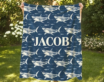May include: A blue fleece blanket with a white shark pattern and the name "Jacob" printed in white in the center.