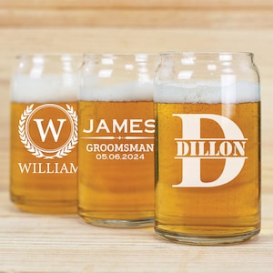 May include: Three personalised beer glasses with a white design. The first glass has a wreath with the letter "W" and the name "William". The second glass has the name "James" and the text "Groomsman 05.06.2024". The third glass has the letter "D" with the name "Dillon" above it.