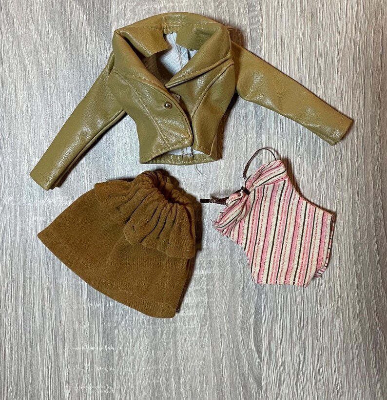 “1960s–70s 1/6 doll outfit with faux leather jacket, suede skirt, and striped top fits Sindy and Blythe.” shown on 1980's Sindy Doll, blonde hair blue eyes. yellow lipstick