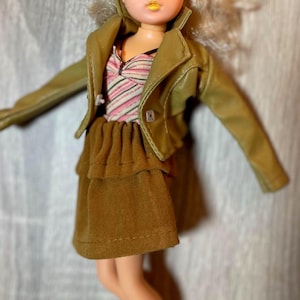 “1960s–70s 1/6 doll outfit with faux leather jacket, suede skirt, and striped top fits Sindy and Blythe.” shown on 1980's Sindy Doll, blonde hair blue eyes. yellow lipstick