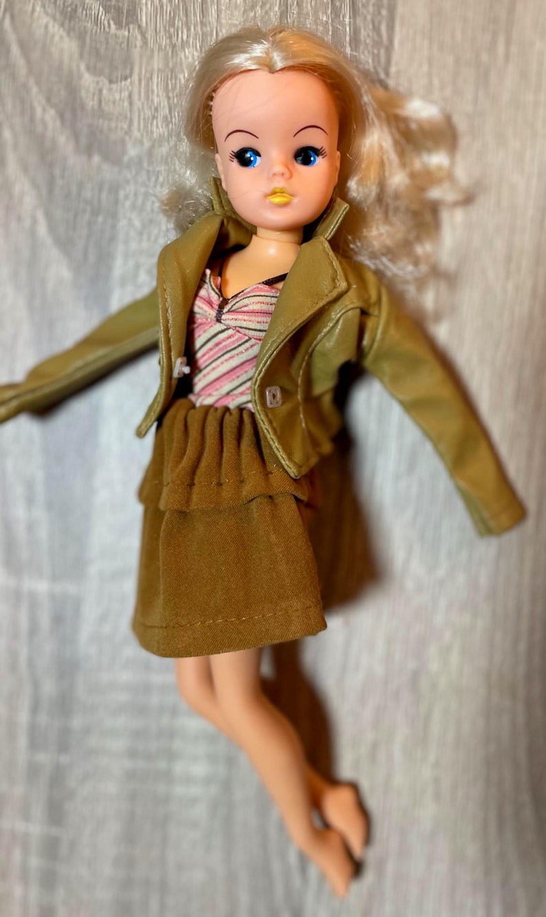 “1960s–70s 1/6 doll outfit with faux leather jacket, suede skirt, and striped top fits Sindy and Blythe.” shown on 1980's Sindy Doll, blonde hair blue eyes. yellow lipstick