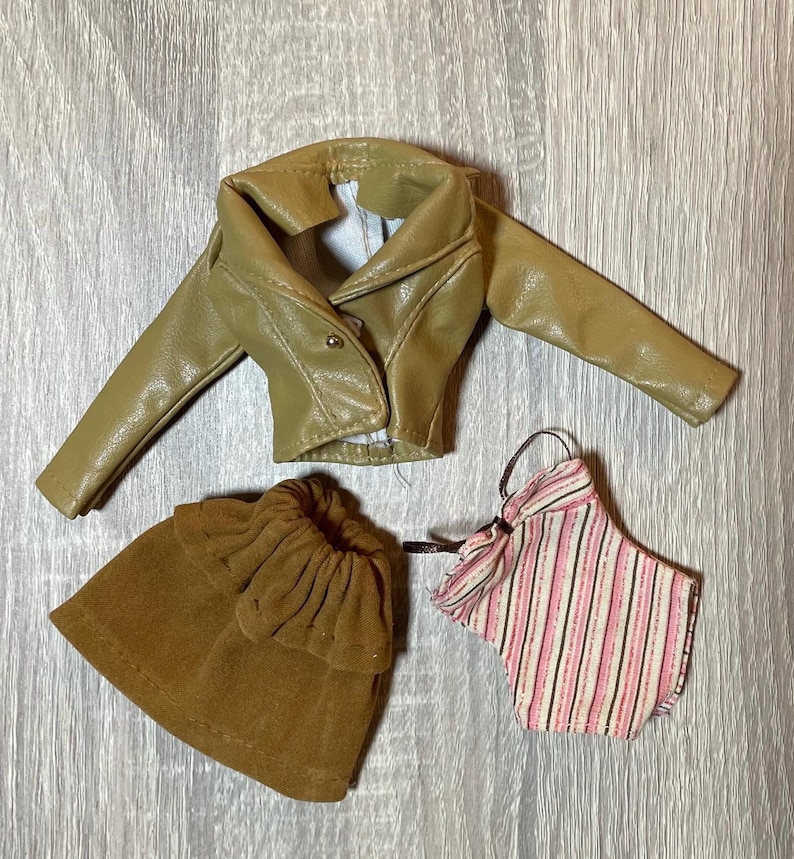 “1960s–70s 1/6 doll outfit with faux leather jacket, suede skirt, and striped top fits Sindy and Blythe.” shown on 1980's Sindy Doll, blonde hair blue eyes. yellow lipstick