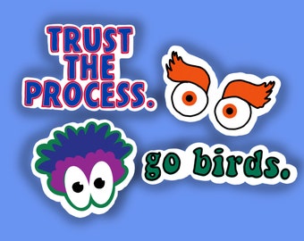 May include: Four colourful stickers with different designs. The first sticker is blue and red and says "Trust the Process." The second sticker is green and says "go birds." The third sticker has two orange eyes with red pupils and orange eyebrows. The fourth sticker has two purple eyes with white pupils and a blue and purple fuzzy head.